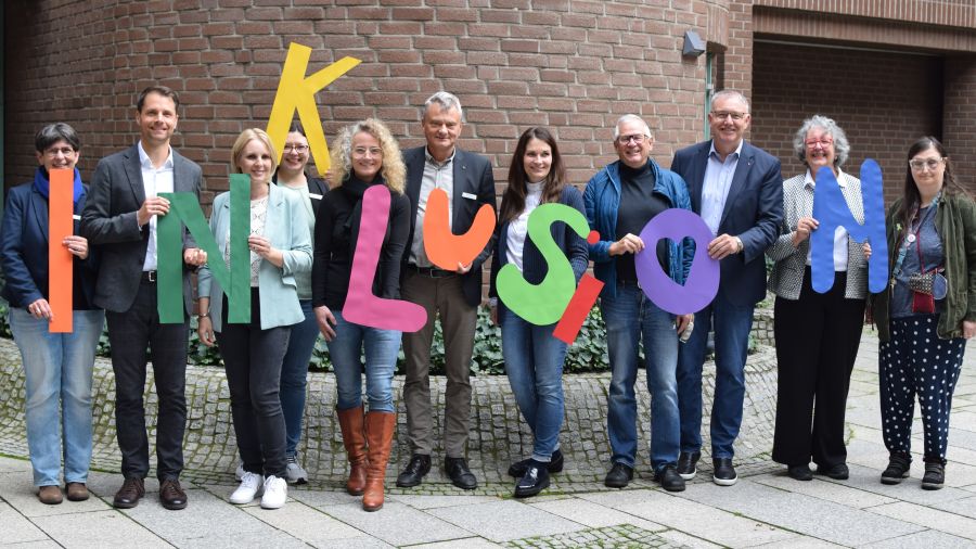 Das Foto zeigt eine Gruppe von Menschen, die das Wort Inklusion in großen bunten Buchstaben hoch halten.