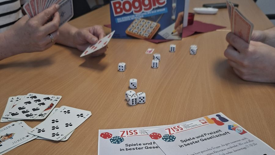 Das Foto zeigt Hände mit Spielkarten und Würfel auf einem Tisch.