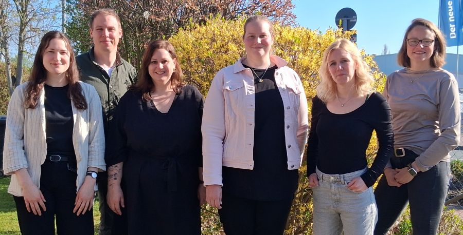 Das Foto zeigt sechs Menschen, die vor einem gelb-blühenden Busch stehen.