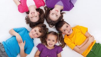 Das Foto zeigt eine Gruppe Kinder. Alle liegen im Kreis auf dem Boden, ihre Köpfe liegen nah aneinander.