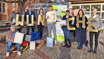 Das Foto zeigt eine Gruppe Menschen, die goldene Buchstaben hochhalten und einige Geschenke. Die Buchstaben bilden das Wort "Wünsche".