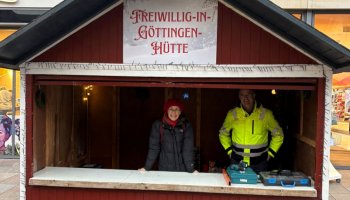 Das Foto zeigt die Vorderseite / Theke einer Weihnachtsmarkthütte. Auf dem Schild im Giebel steht „Freiwillig-in-Göttingen-Hütte“.