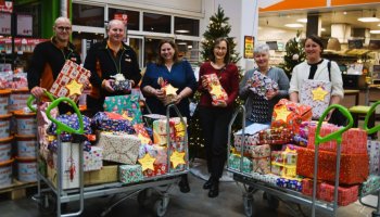 Das Foto zeigt die Mitarbeitenden von Globus Baumarkt und Caritas mit zwei großen Transportwagen voller Geschenke, alle halten ein Geschenk in der Hand.