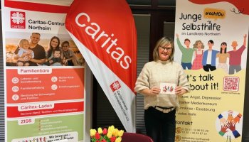 Das Foto zeigt Anna Holland an zwischen zwei Roll-Ups und einer Beach-Flag an einem Messestand.