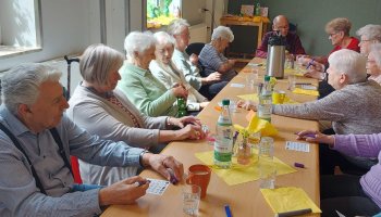 Viele Menschen sitzen an einem langen Tisch und spielen Bingo.