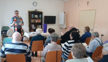 Das Foto zeigt Menschen auf Stühlen, vorne steht der Propst und spricht.