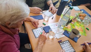 Ein Tisch mit mehreren Bingo-Karten und Händen von Spielenden.