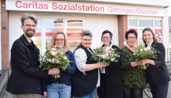 Das Bild zeigt ein Gruppebild mit Blumensträußen vor der Caritas-Sozialstation Göttingen / Gleichen.