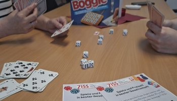 Das Foto zeigt Hände mit Spielkarten und Würfel auf einem Tisch.