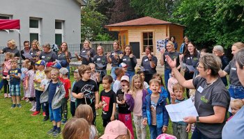 Das Foto zeigt eine Gruppe Kinder beim Singen, im Hintergrund ein Gartenhaus.