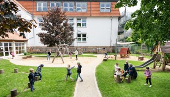Das Foto zeigt spielende Kinder auf dem Campus-Gelände, im Hintergrund Gebäudeteile.