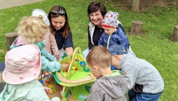 Das Foto zeigt Krippenkinder rund um einen Spieltisch auf einer Wiese.