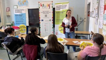 Tina Otto gibt Informationen an vier Personen, die im Vordergrund sitzen.
