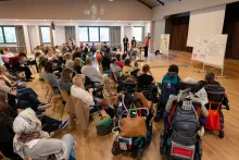 Menschen sitzen im Halbkreis, einige im Vordergrund auf eigenen Rollstühlen.