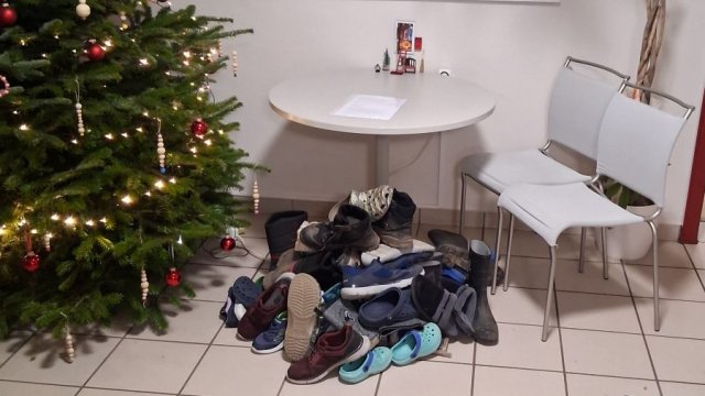 Das Foto zeigt einen Haufen Schuhe neben einem Weihnachtsbaum.