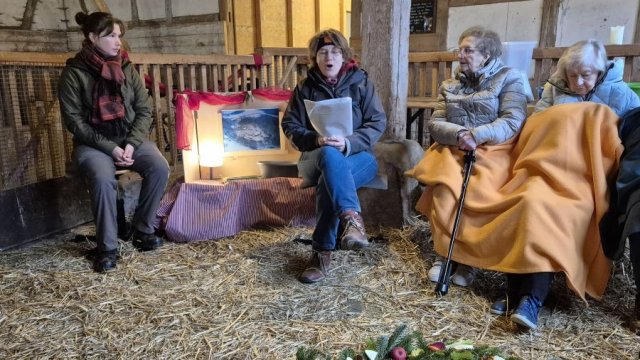 Das Foto zeigt vier Menschen, die im Stall sitzen, der Boden ist mit Stroh bedeckt.