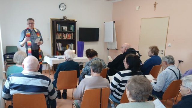 Das Foto zeigt Menschen auf Stühlen, vorne steht der Propst und spricht.