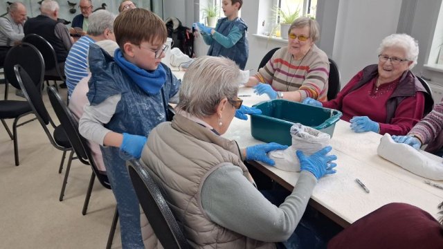 Das Foto zeigt, wie Kinder älteren Menschen beim Gipsen helfen.