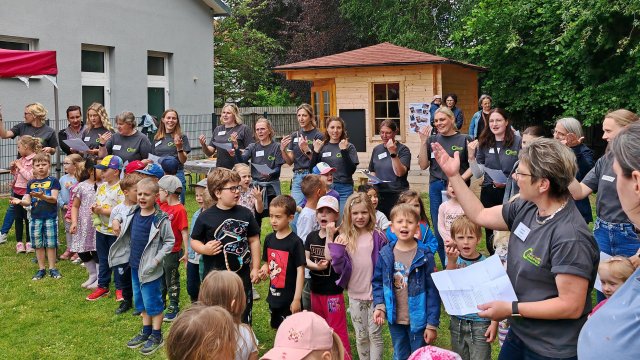 Das Foto zeigt eine Gruppe Kinder beim Singen, im Hintergrund ein Gartenhaus.