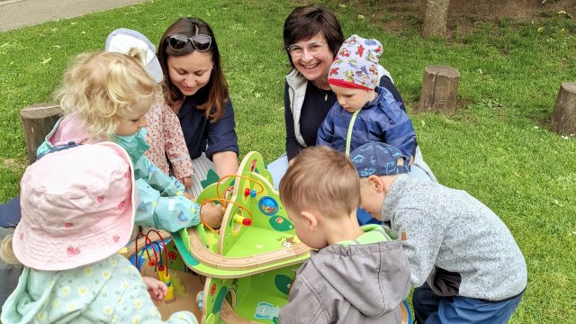 Das Foto zeigt Krippenkinder rund um einen Spieltisch auf einer Wiese.