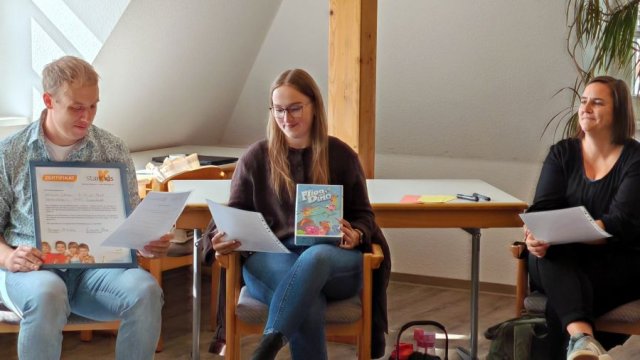 Drei Personen sitzen und betrachten Material.