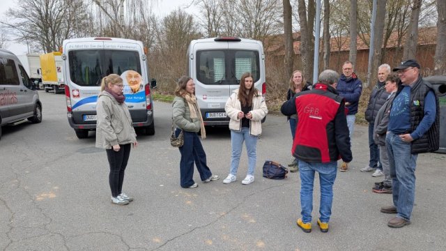 Das Foto zeigt eine Besprechung von stehenden Menschen vor drei Kleinbussen.