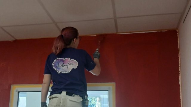 Eine Handwerkerin ist von hinten zusehen. Sie malert.