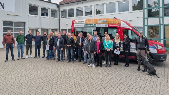 Das Foto zeigt eine Gruppe von Menschen vor einem roten Minibus.