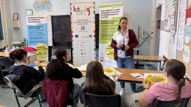 Tina Otto gibt Informationen an vier Personen, die im Vordergrund sitzen.