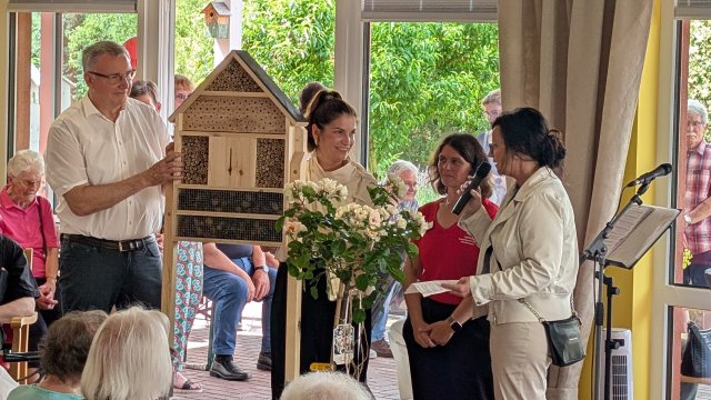 Das Foto zeigt  Menschen mit einem Insektenhotel und einem Rosenstrauch.
