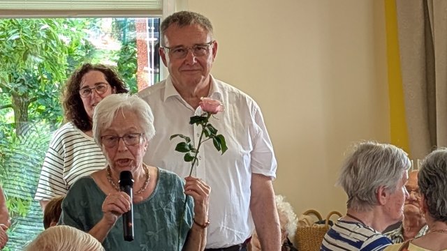 Das Foto zeigt eine Frau, die in eine Mikrofon spricht, dahinter steht ein Mann.