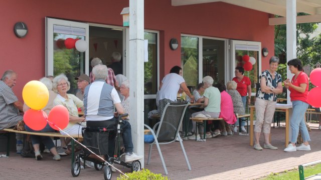 Das Foto zeigt Menschen, die im Schatten auf einer Terrasse sitzen.