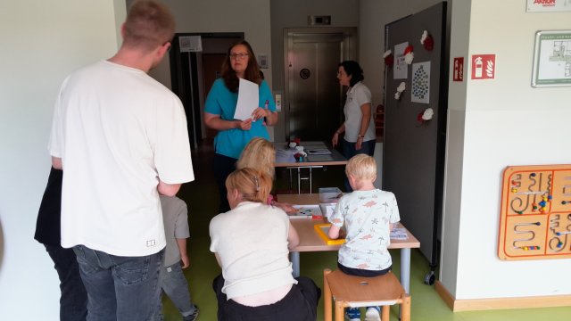 Menschen stehen und Kinder sitzen rund um einen Tisch